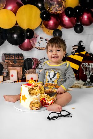 Child at birthday party table with balloons and cake, wearing gray sweatshirt and smiling.