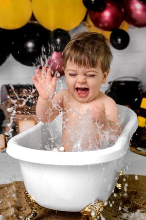 A joyful child splashes and plays in a white bathtub creating a dynamic water spray effect against a dark background.