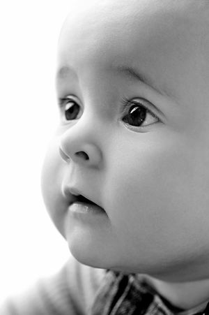 Black and white close-up portrait of a baby with large expressive eyes looking up with wonder.