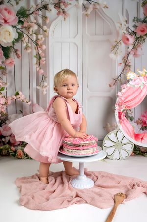 Pink floral cake smash photography session featuring a white backdrop and delicate cherry blossom decorations.