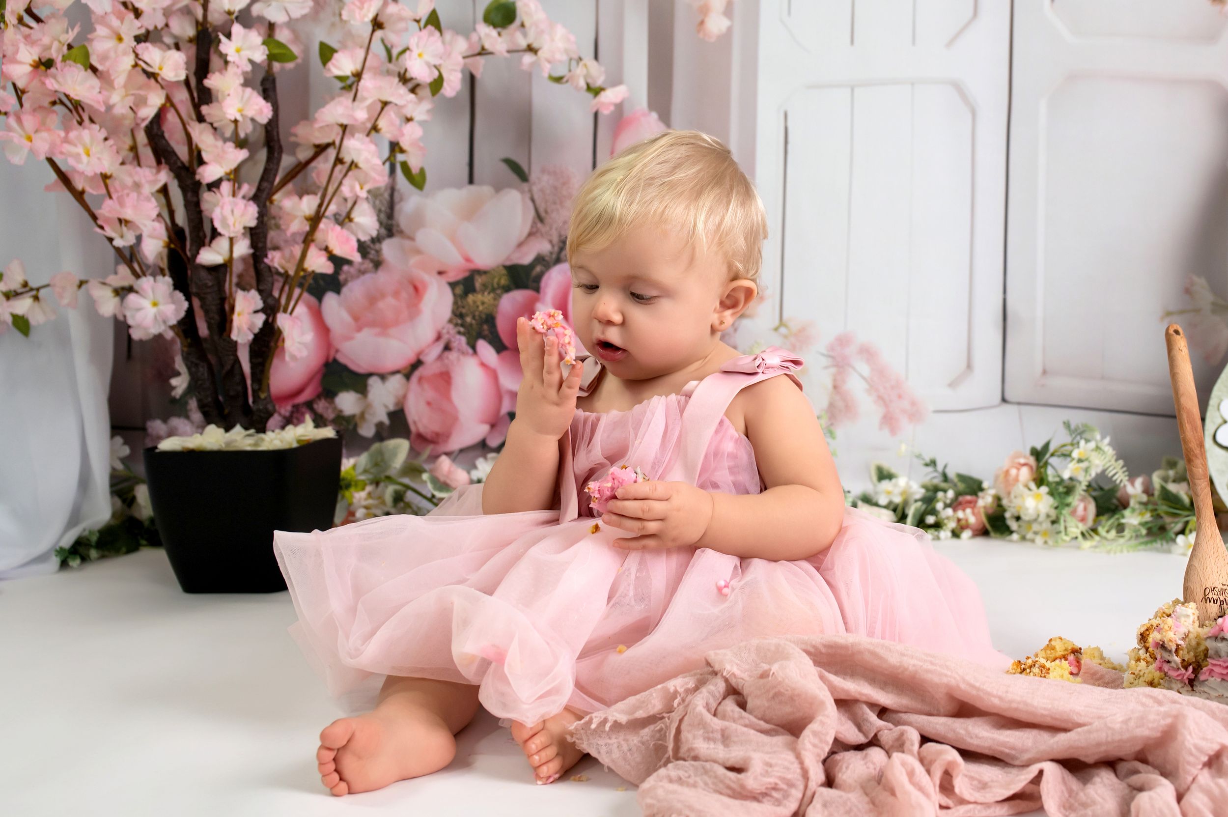 A baby in a pink tutu dress sits among cherry blossom decorations during a spring-themed photo session.