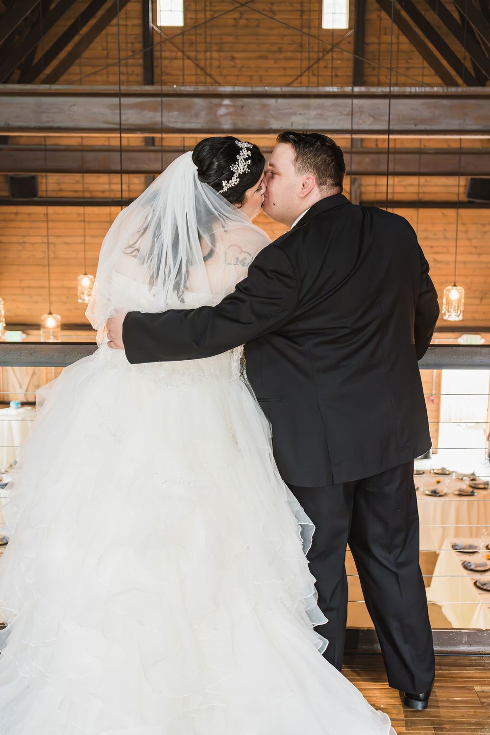 A bride and groom share an intimate dance moment in a rustic venue with exposed wooden beams and warm lighting.