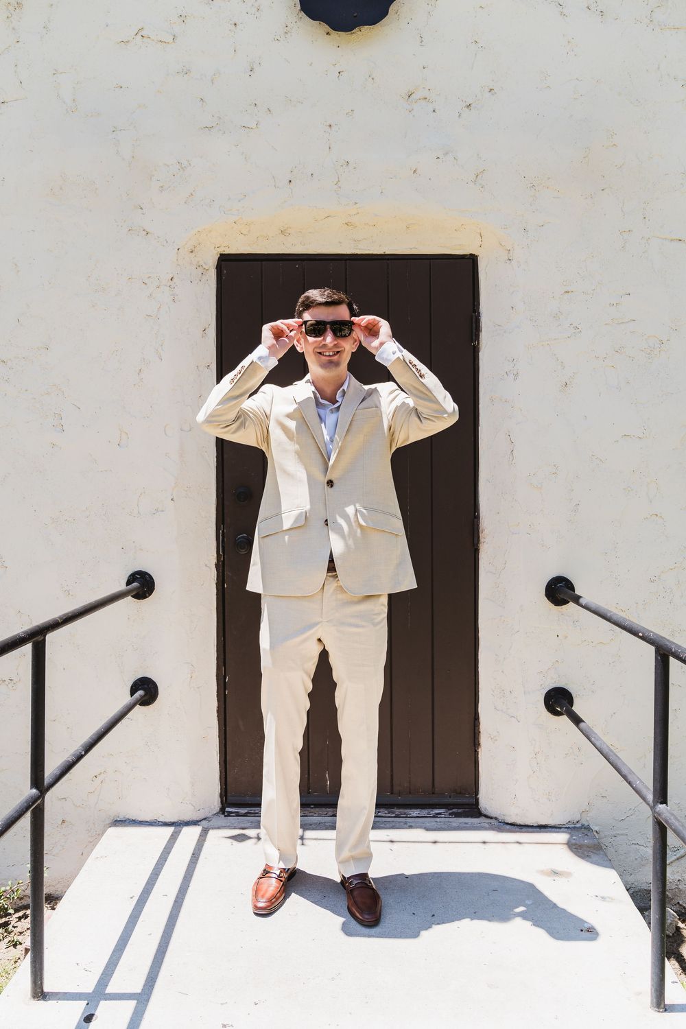 A playful sequence showing a person in a beige suit making silly poses against a white wall with dark doors.