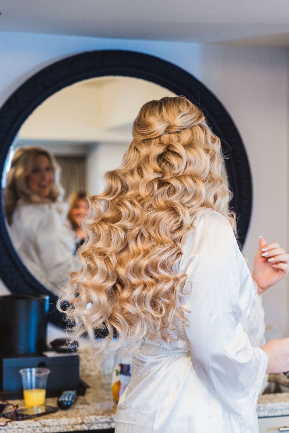 Blonde curly hair being styled in a series of preparation shots with a white robe and mirror reflections.