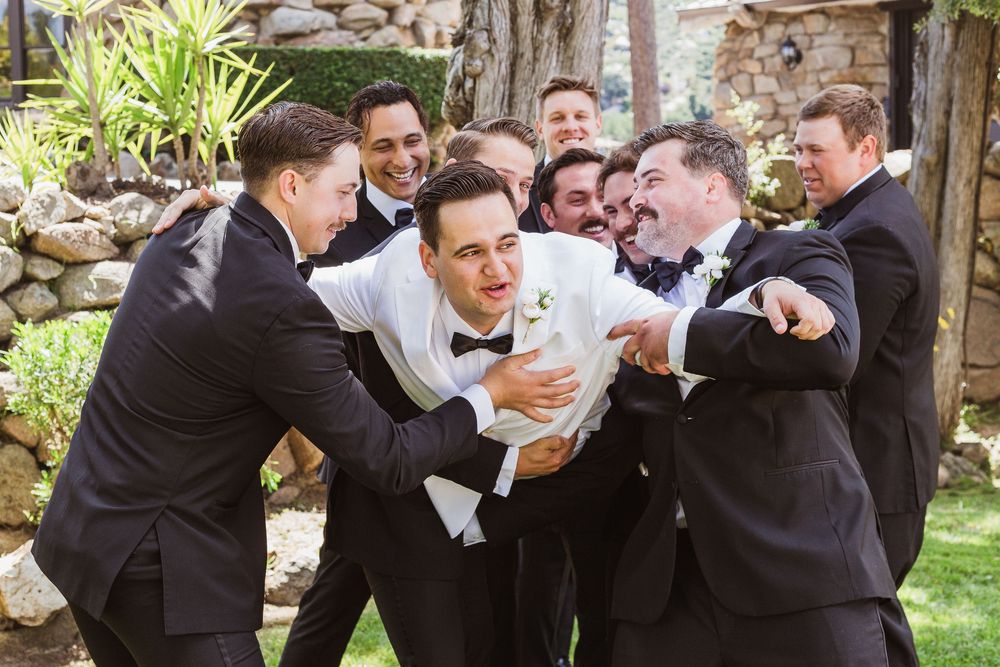 Group in formal attire celebrating and laughing together outdoors in a garden setting.
