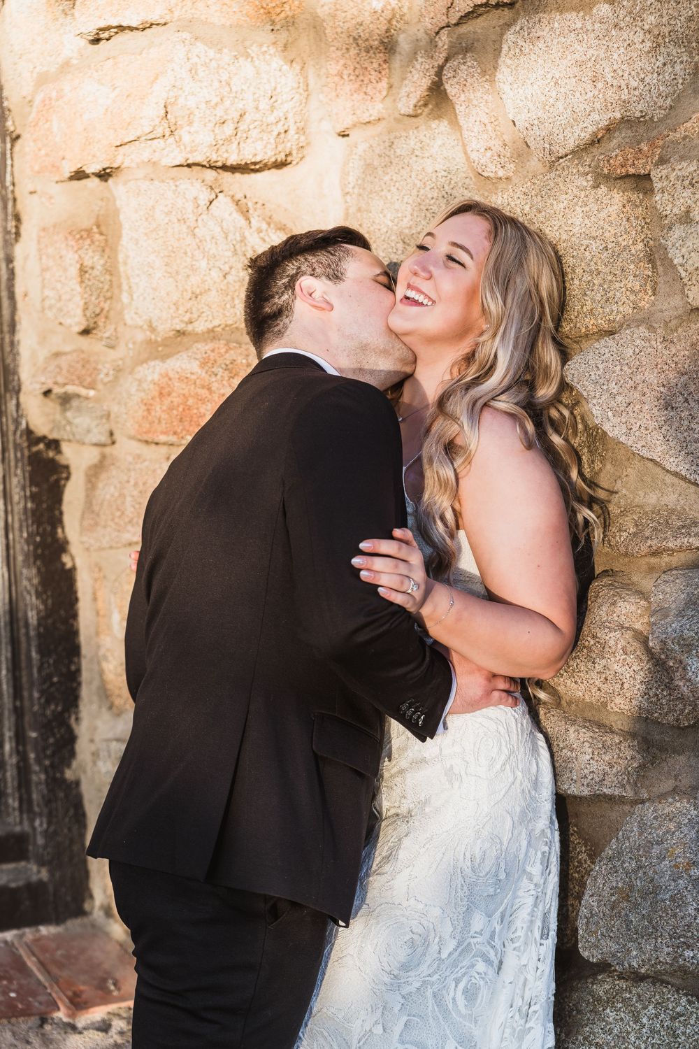A romantic moment between newlyweds against a rustic stone wall backdrop.