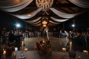 A wedding reception venue with draped fabric ceilings, chandeliers, and tables set for an elegant evening celebration.