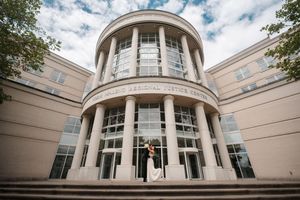 Couple poses on steps of a grand neoclassical justice center building with columns and large windows.