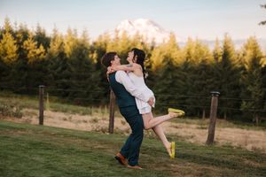 Groom lifting bride in white dress with yellow shoes, green trees and Mount Rainier in background at golden hour.