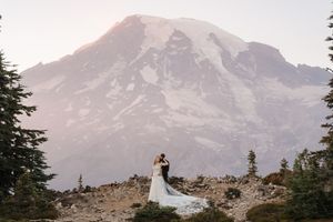 Bride and groom embrace before snow-capped Mount Rainier at sunset during outdoor mountain elopement wedding.
