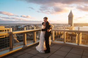 Couple embraces on rooftop terrace overlooking city skyline at sunset with dramatic cloudy sky.