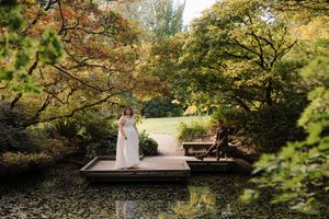 A couple sits on a wooden bench surrounded by autumn foliage in a serene garden setting.