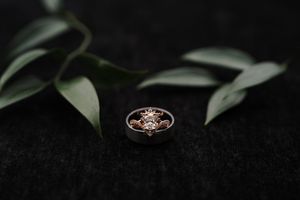 Rose gold floral diamond ring resting on dark velvet surface with green leaves in background.