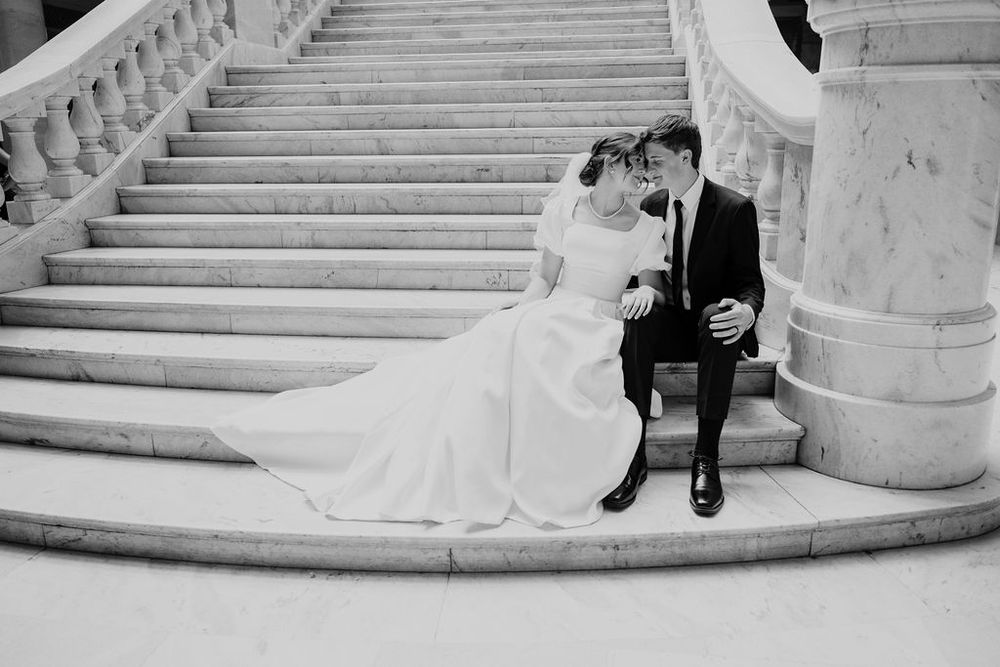 Black and white photo of bride and groom sitting on curved marble steps.
