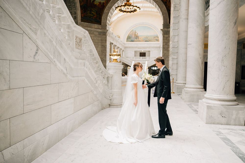 Wedding couple share intimate moment among marble columns in grand hall.