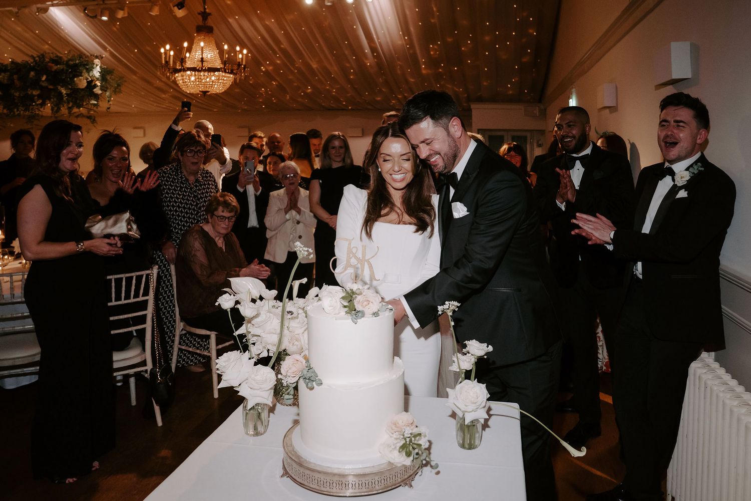 bride and groom cutting cake surrounded by cheering wedding guests at Iscoyd park
