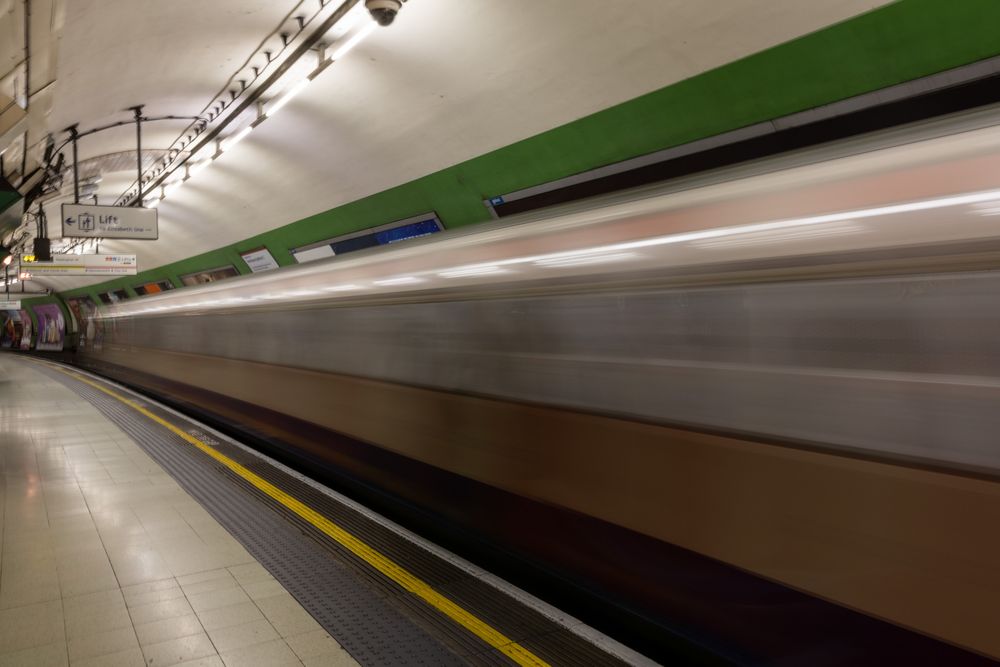 Time-lapse photograph showing motion blur of a subway train arriving at an underground station with green accents.