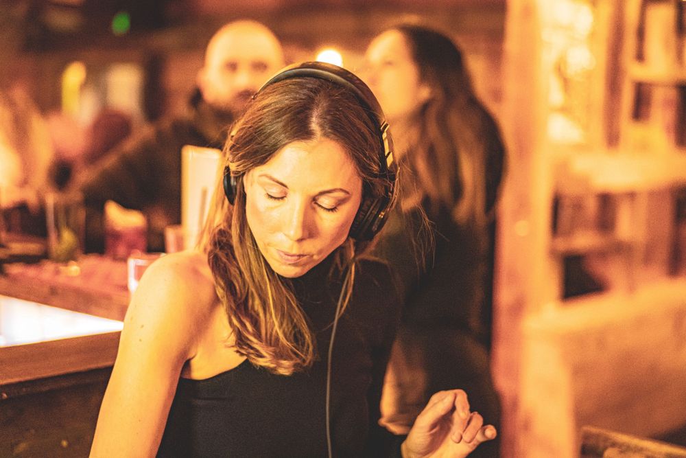 A person focuses intently while mixing drinks behind a dimly lit bar with warm ambient lighting.