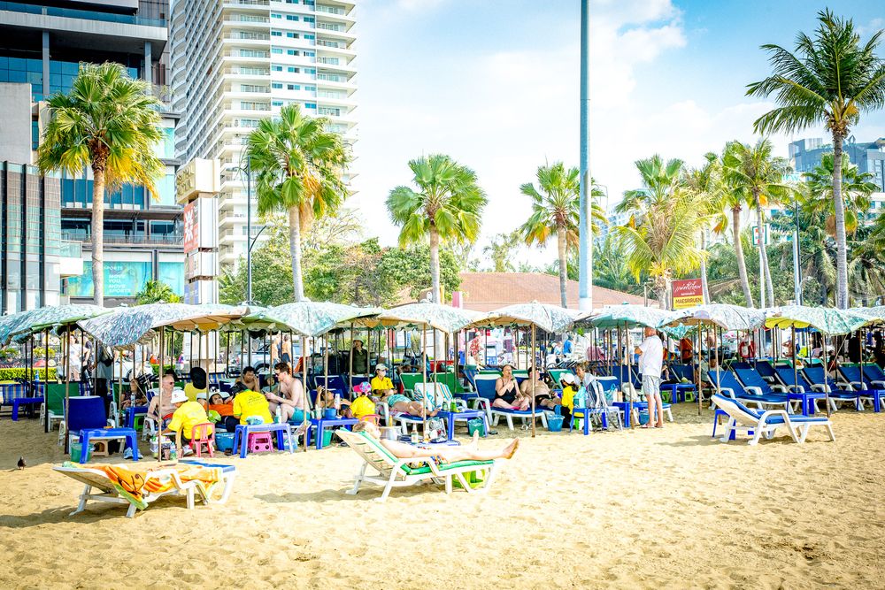 Panoramic view of a sunny beach with palm trees, high-rise buildings, and colorful beach umbrellas along the shoreline.