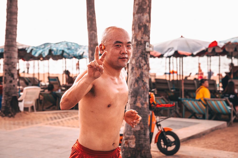 Shirtless man performs a series of dynamic martial arts moves in an outdoor beach setting at sunset.