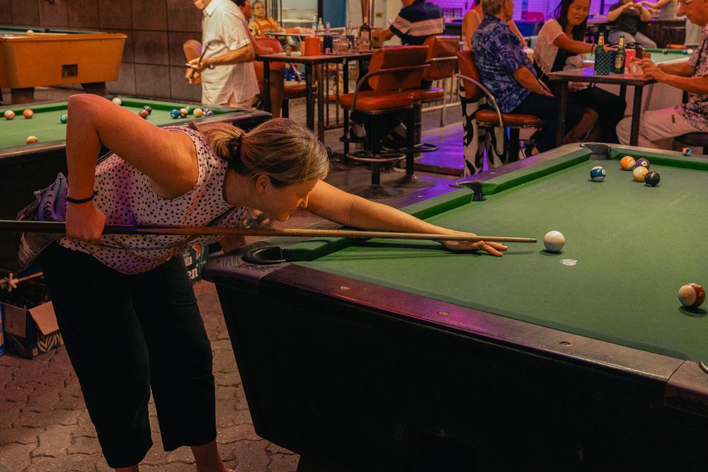 A player leans over a pool table to make a shot in a colorful game room with multiple billiards tables.
