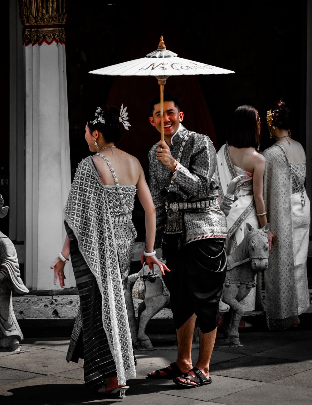 People walking under a white umbrella casting dramatic shadows on a sidewalk in black and white photography.