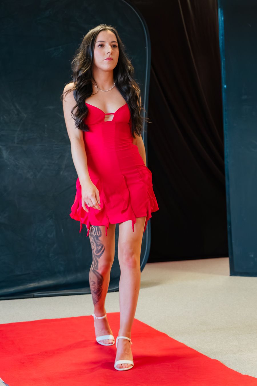 Model in red sleeveless dress strikes dynamic poses on red carpet during photo session.