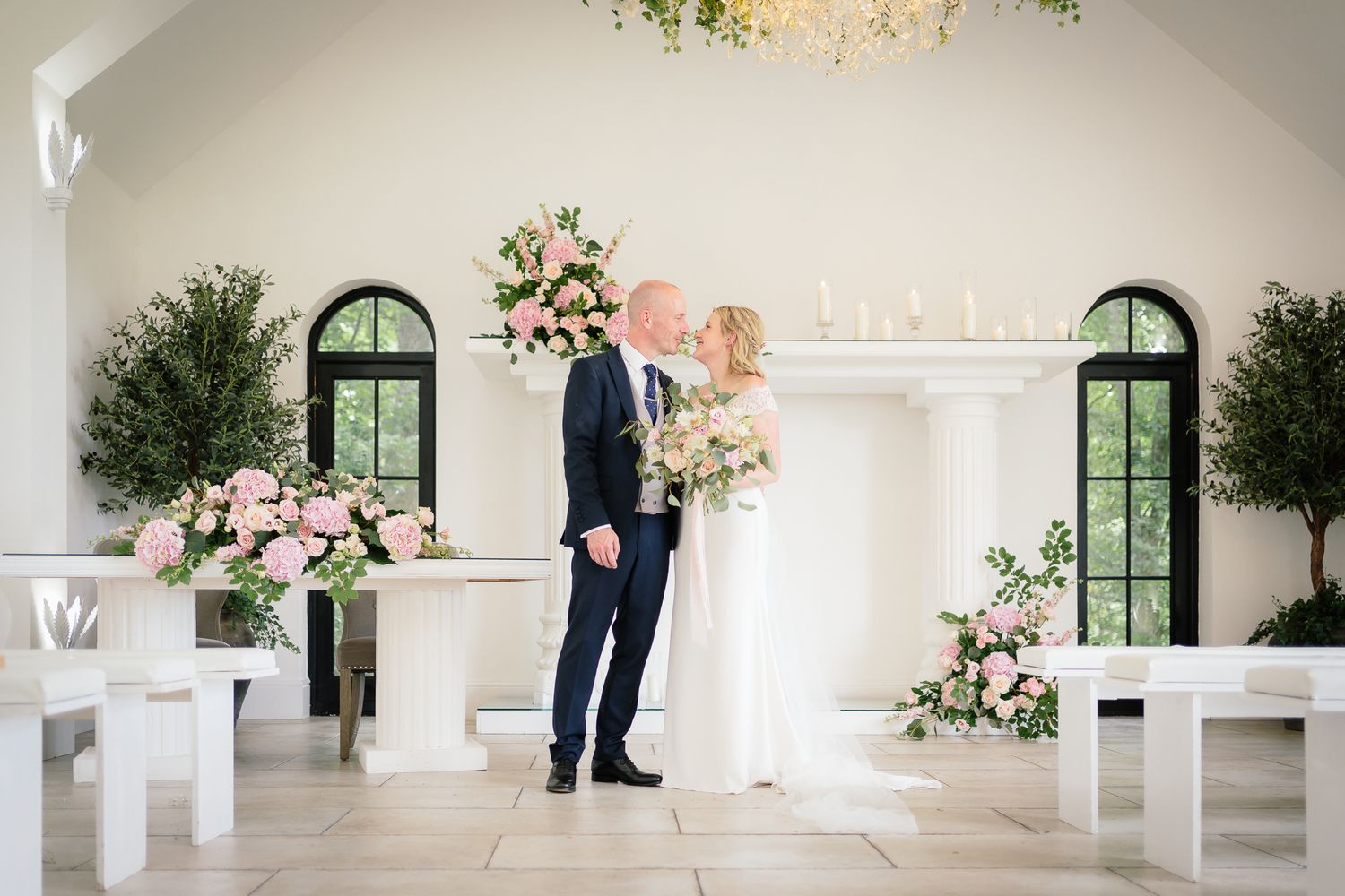 Bright white wedding venue interior with elegant floral arrangements and arched windows. Woodhill Hall.