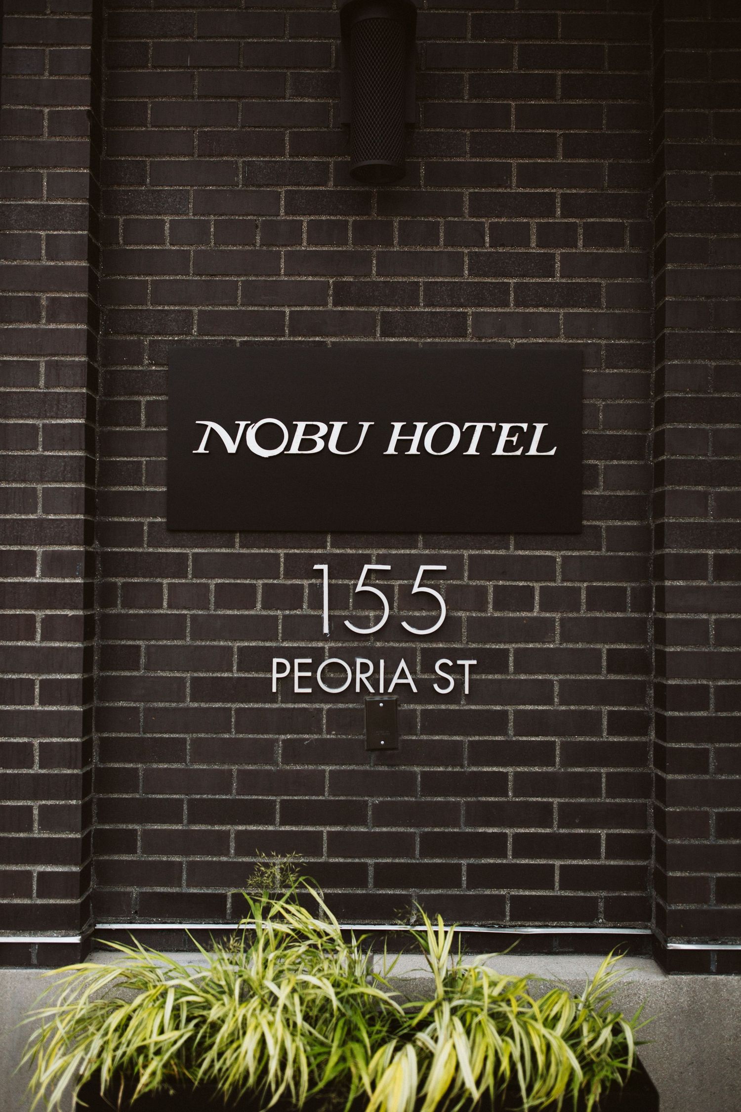 Nobu Hotel signage on brick wall at 155 Peoria Street with ornamental grass.