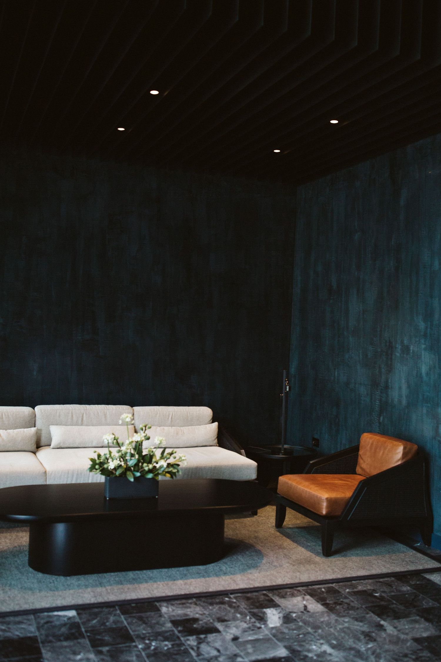 Modern lounge area with white sofa and leather chair against dark blue walls.