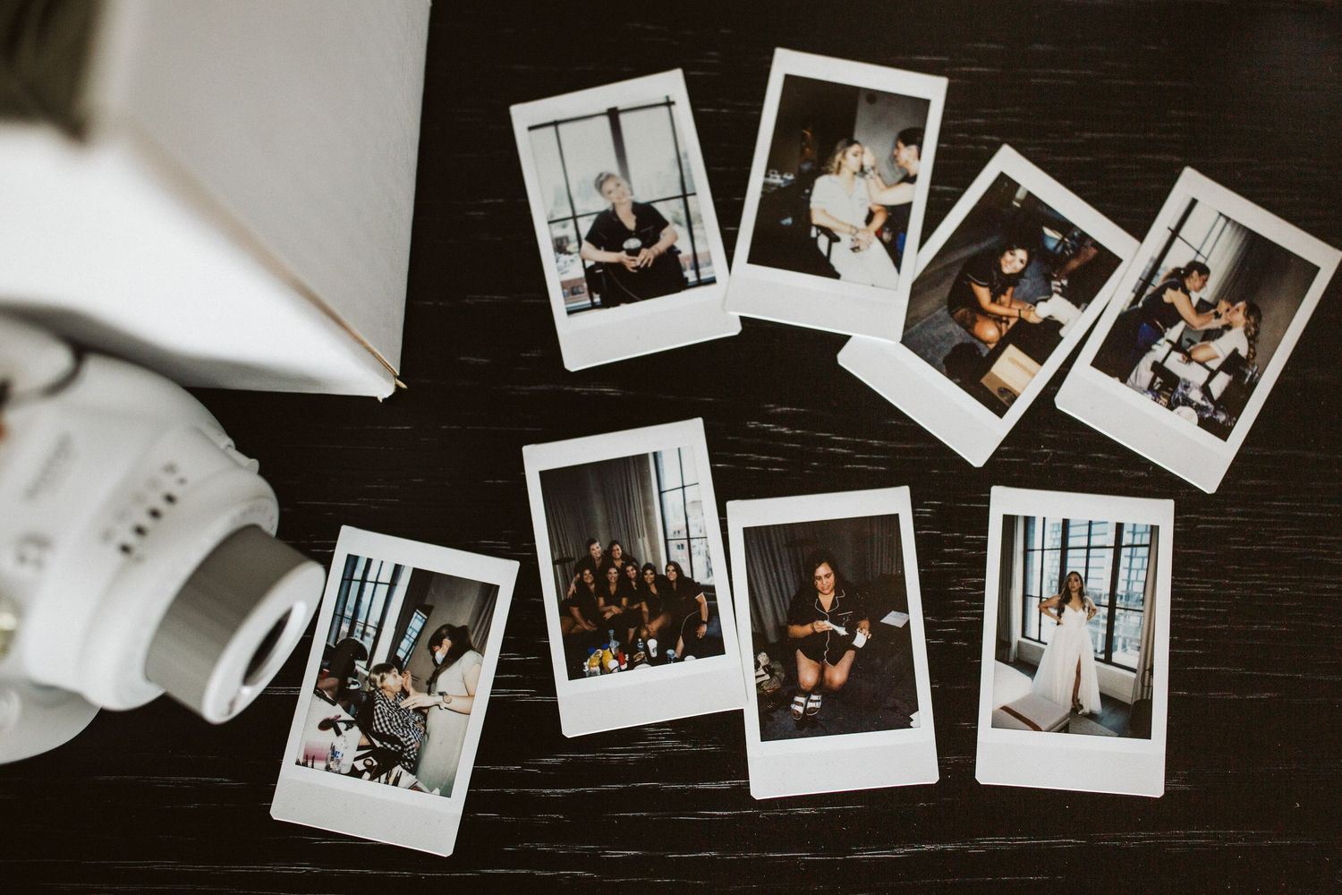 Collection of polaroid photos spread out on dark surface next to instant camera.