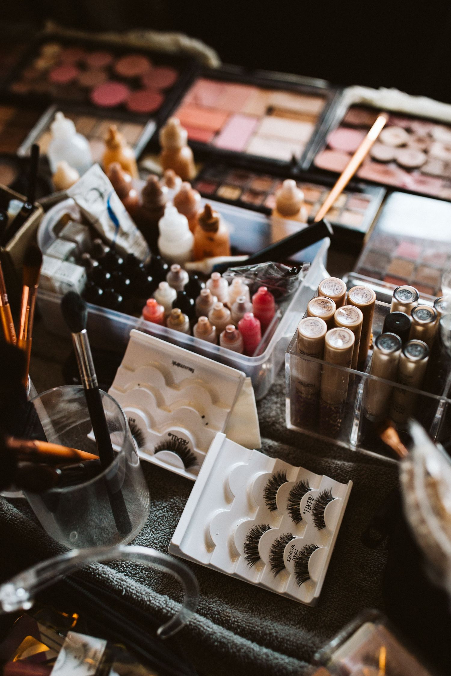 Professional makeup kit with false eyelashes, brushes and cosmetics arranged on dark surface.