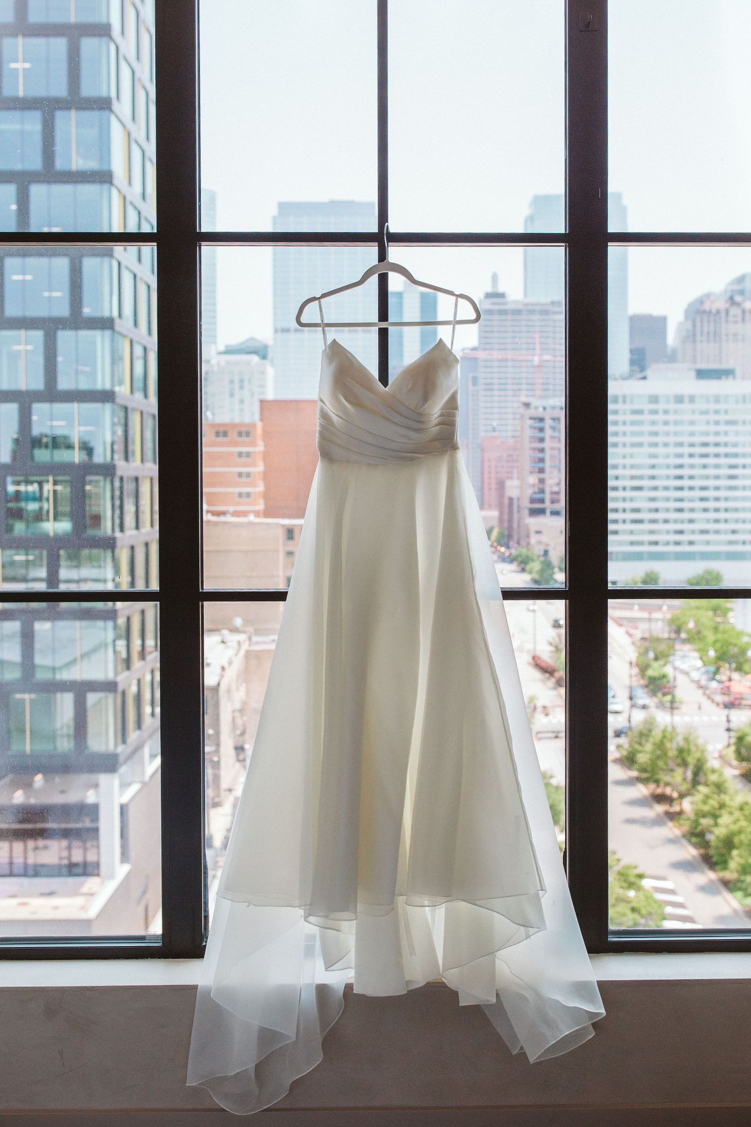White wedding dress hanging in front of city windows with urban skyline view.