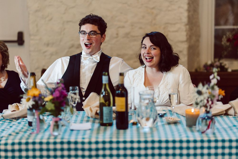 Couple shares a joyful moment at their wedding reception with blue checkered tablecloth and wine bottles on table.