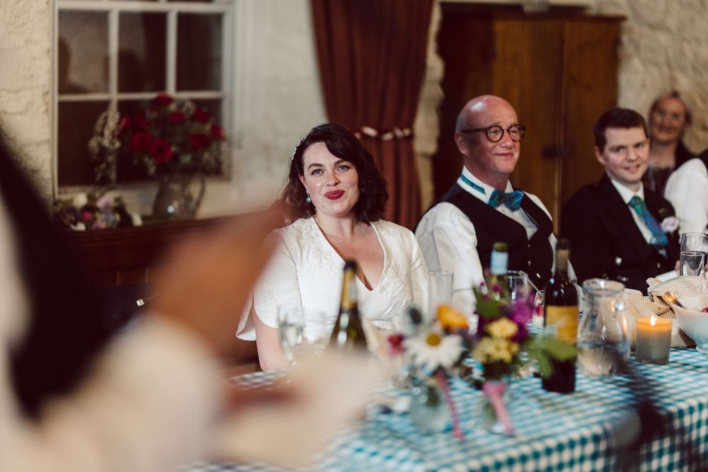 Guests seated at a wedding reception table with floral centerpieces and checkered tablecloths.