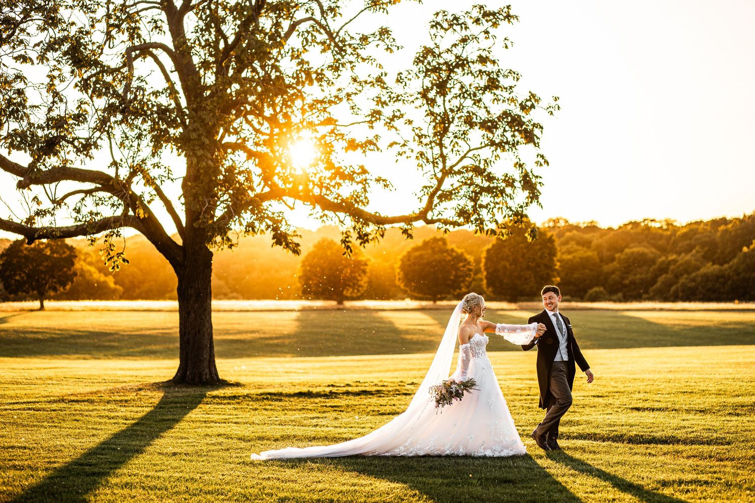Romantic bride and groom walking hand in hand on lush green lawn during golden sunset wedding photography.
