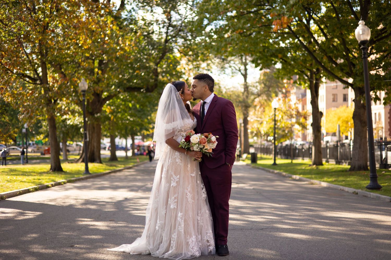 Newlyweds share romantic moments in a sunlit autumn park setting with golden leaves and trees in the background.