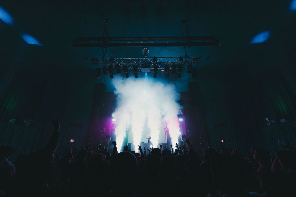 Silhouetted performers on stage with dramatic blue and white lighting effects during a concert performance.
