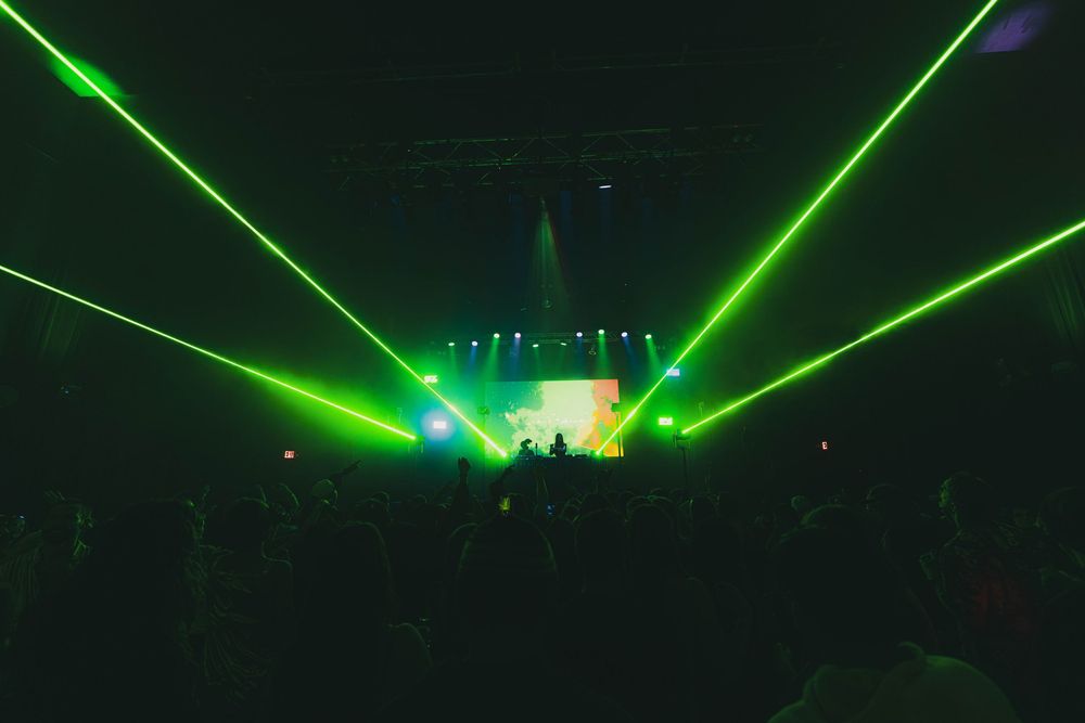 Green laser beams illuminate a dark concert venue during an energetic live performance.