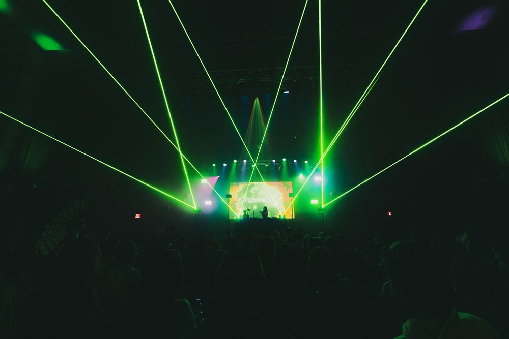 Bright green laser beams illuminate a concert stage with dramatic lighting effects during a live performance.