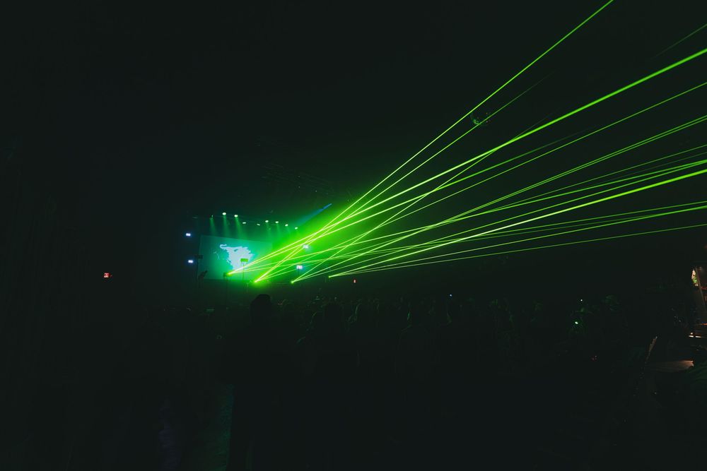 Green laser beams illuminate the night sky during an outdoor light show performance.