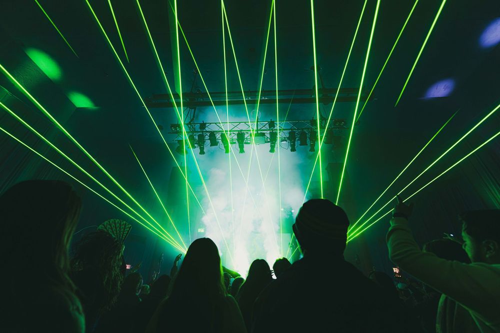 Green laser beams illuminate a dark concert venue with atmospheric fog effects creating dramatic lighting patterns.