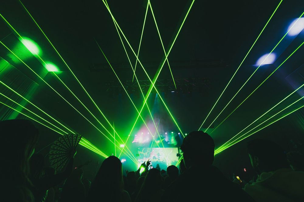 Green laser beams illuminate a dark nightclub atmosphere during an energetic dance party performance.