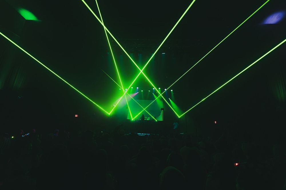 Green laser beams create dynamic patterns across a dark performance space during an electronic music show.