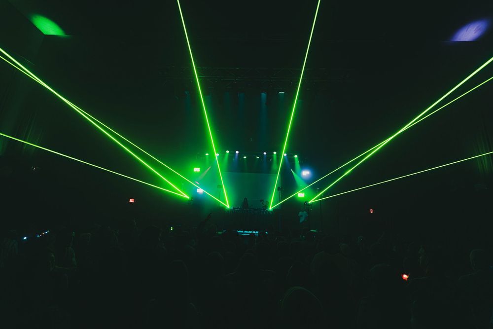 Vibrant green laser lights form symmetrical patterns against a black background in a concert venue.
