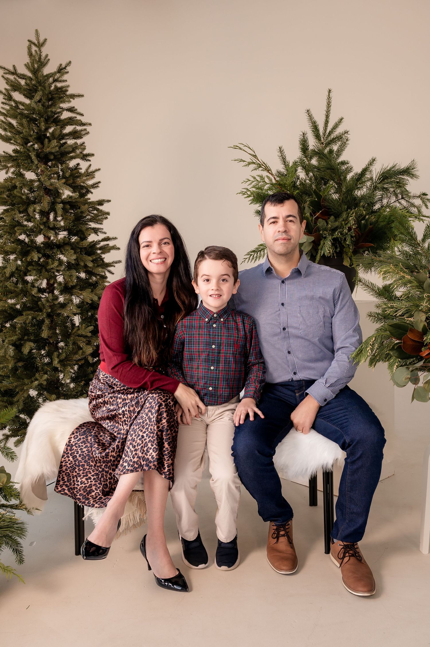 A family poses for a holiday portrait in front of decorated Christmas trees in a studio setting.