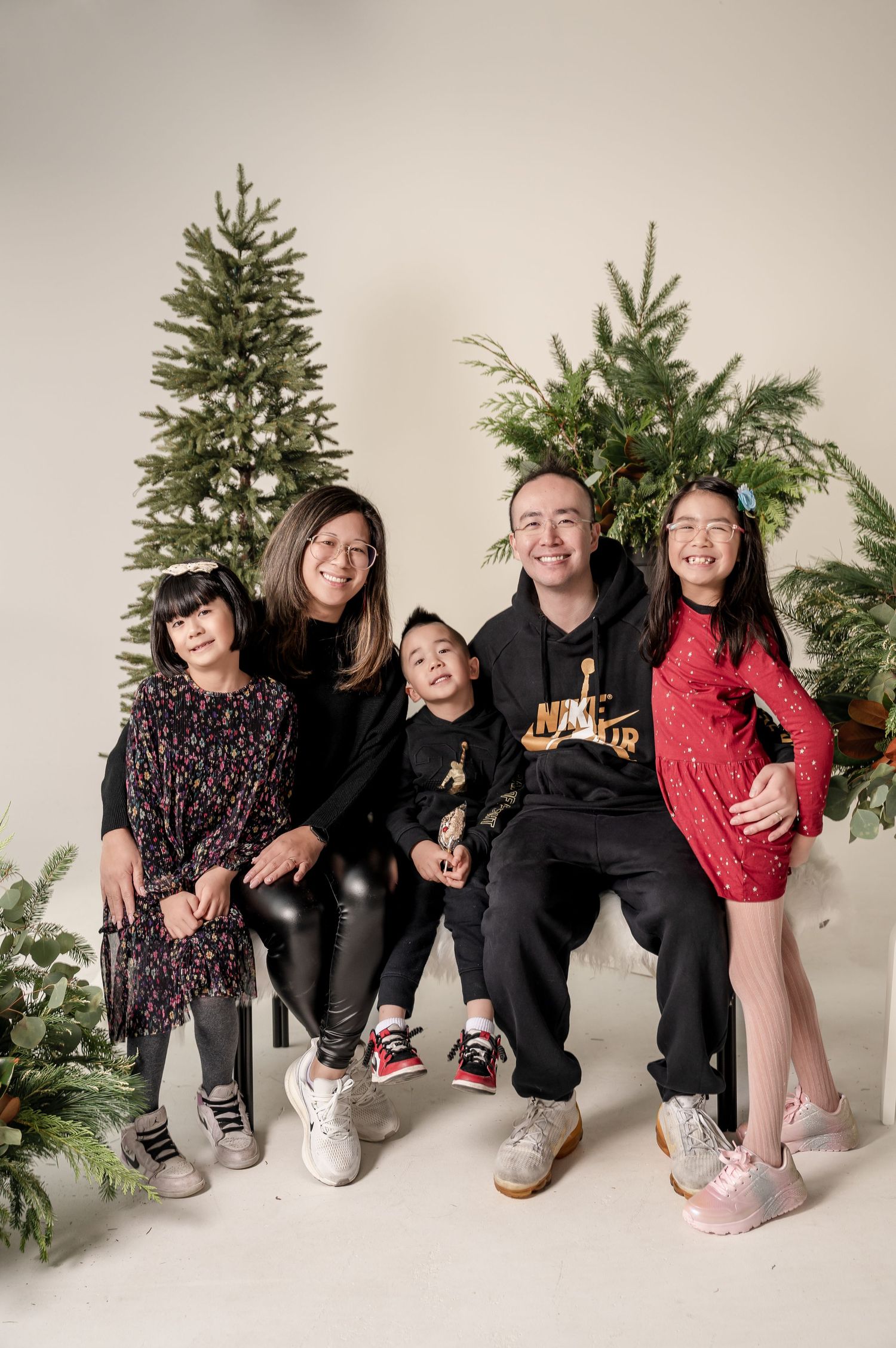 A playful group poses in front of Christmas trees for a festive holiday photo series against a light backdrop.