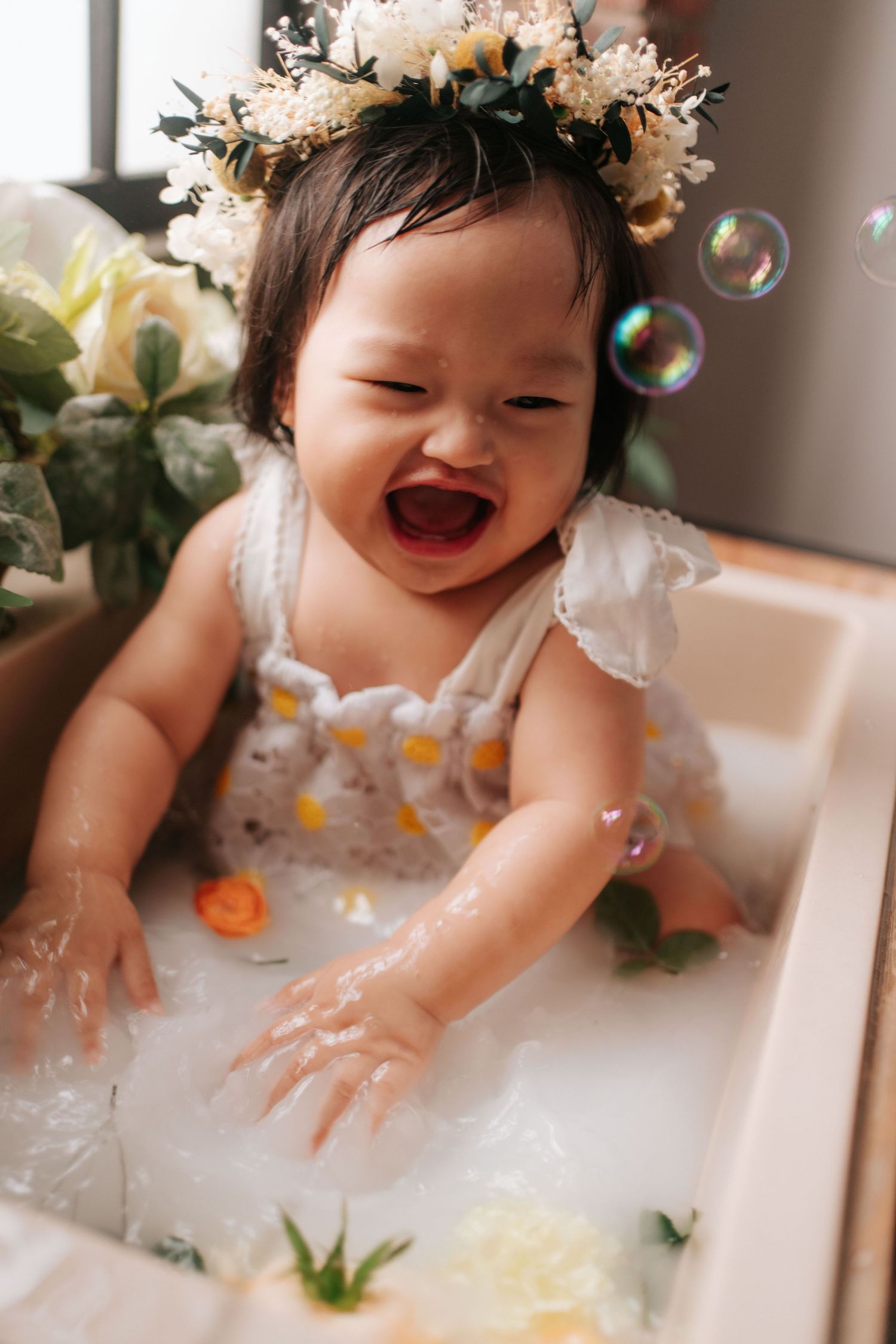 A baby cake smash photo session with white balloons, pampas grass, and rustic wood backdrop for first birthday celebration.