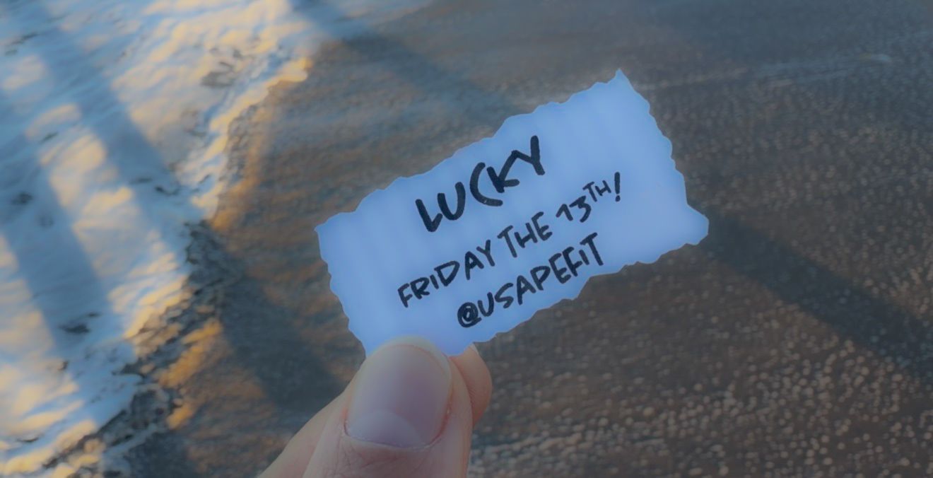 Hand holding a small piece of paper with writing against a blurred mountainous background at sunset.