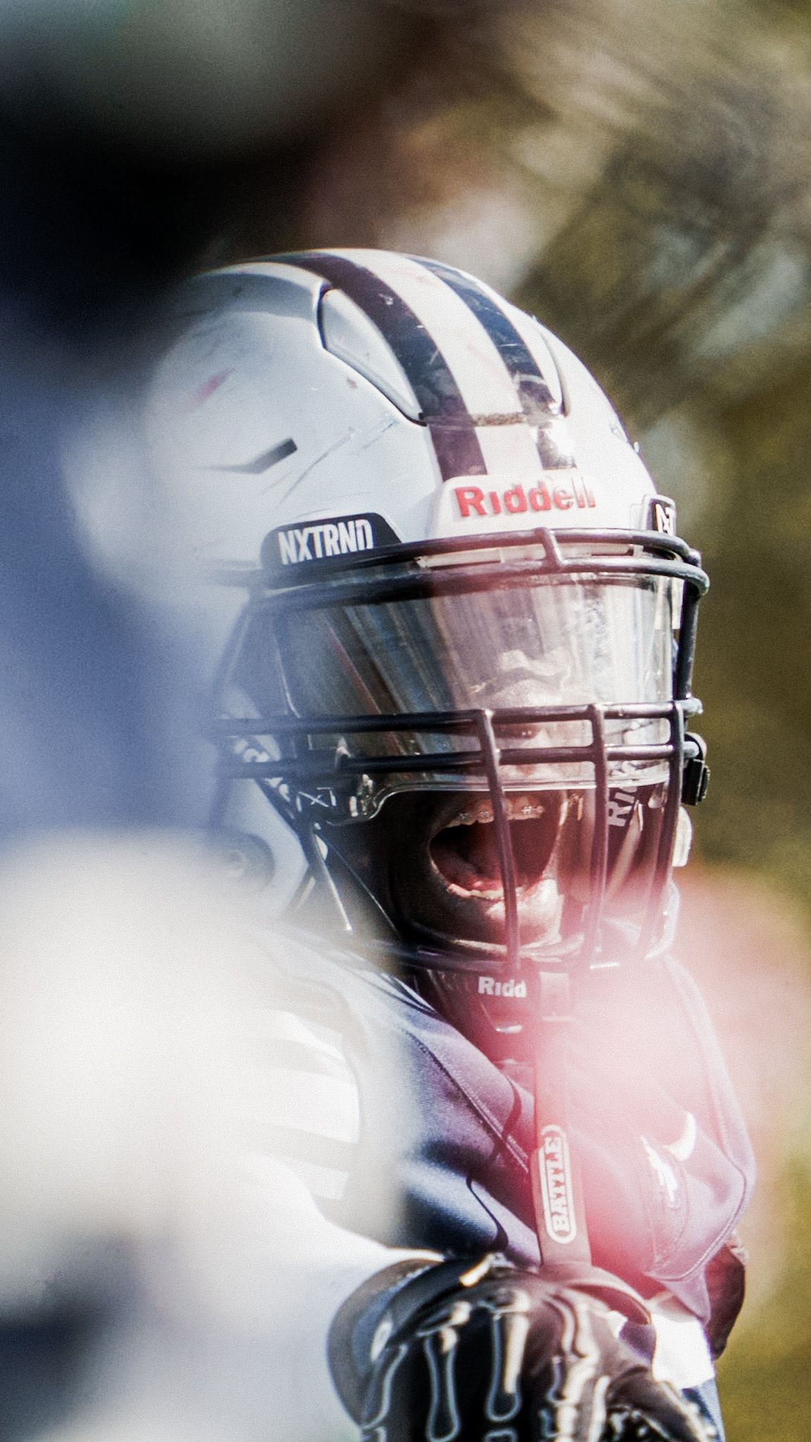 A football player wearing a white Riddell helmet with dark face mask and NXTRND branding in intense game focus.
